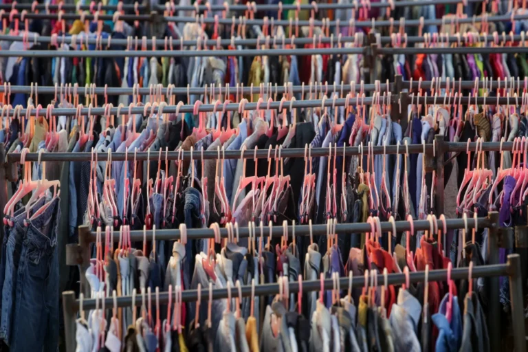 Gran cantidad de prendas de ropa de mujer y hombre colgadas en perchas de color rosa representando la moda rápida o fast fashion