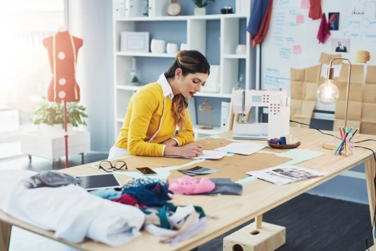 Diseñadora trabajando en modelos de producción en moda con patrones y materiales en un taller de costura.