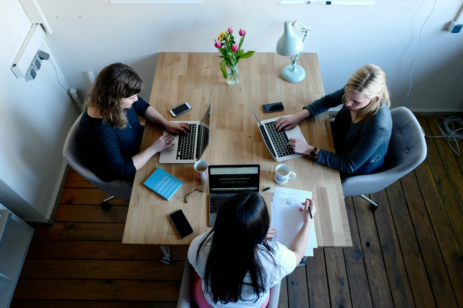 Tres mujeres trabajando en equipo con portátiles y cuadernos alrededor de una mesa, representando colaboración y habilidades blandas en el entorno laboral